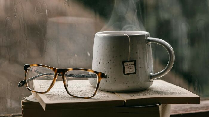 Reading glasses resting on an open book next to a steaming mug, evoking high school literature knowledge.