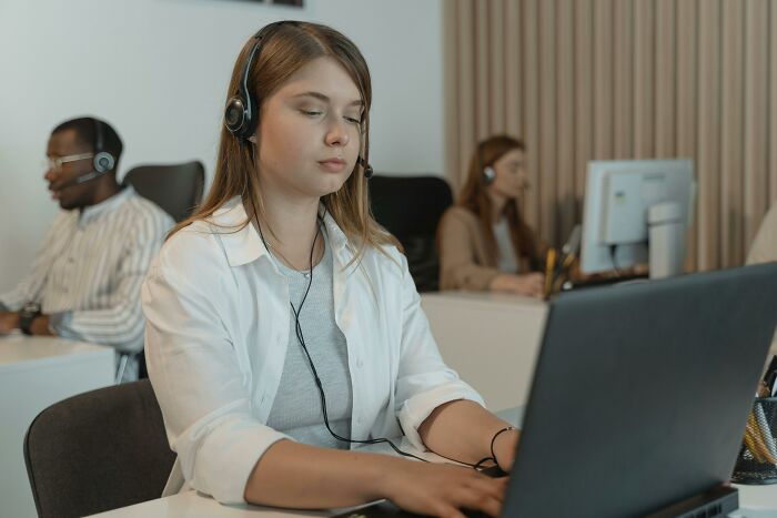 Young female employee wearing headset working on laptop in office sharing dark dirty truths about industries.