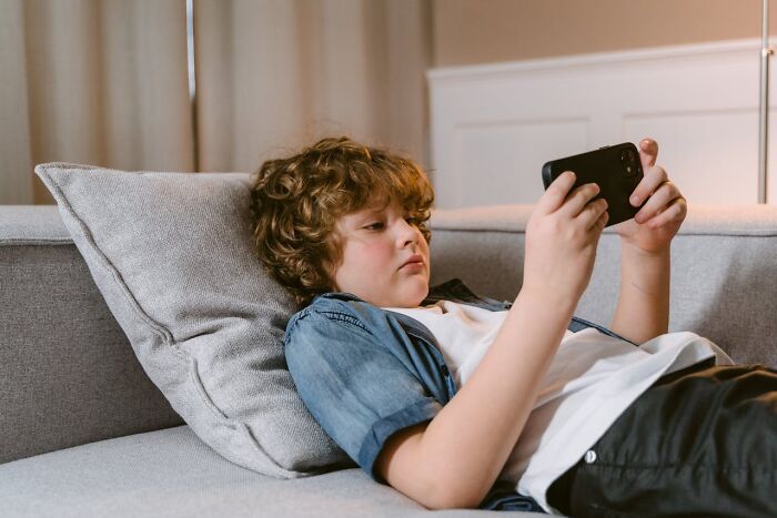 Young boy lying on a couch using a smartphone, illustrating modern parenting trends and technology use in families.