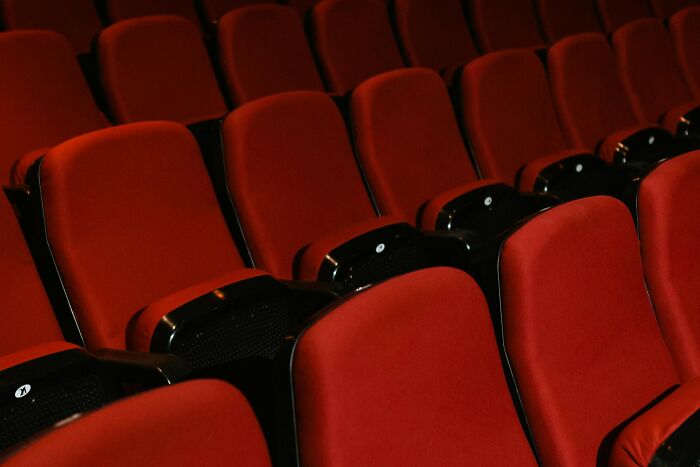 Empty red movie theater seats in a dimly lit cinema, inviting viewers to guess famous films from opening scenes. Empty red movie theater seats in a dimly lit cinema, inviting viewers to guess famous films from opening scenes.
