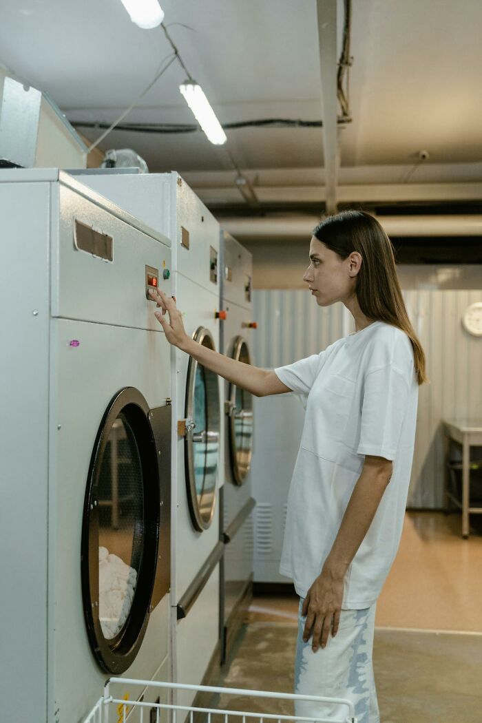 Young woman using a laundromat washing machine, showcasing a glitch in the system opportunity being exploited.
