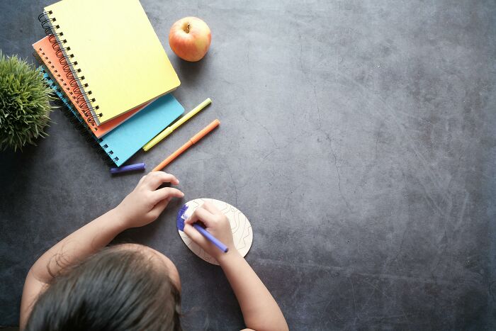 Child drawing with colored markers near notebooks and apple, illustrating top IQ exams and brain challenge activities in the UK.