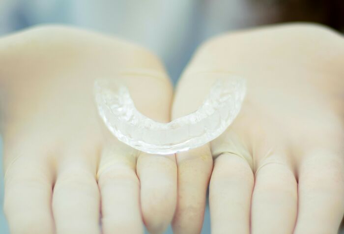 Close-up of hands wearing gloves holding a clear dental mouthguard symbolizing unresolved mysteries people carry with them.