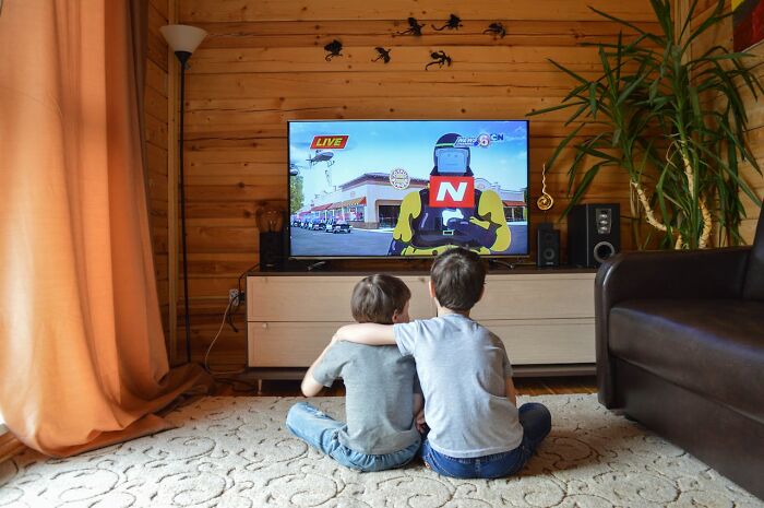 Two kids sitting on carpet watching modern parenting trends featured on TV in a cozy wood-paneled living room.