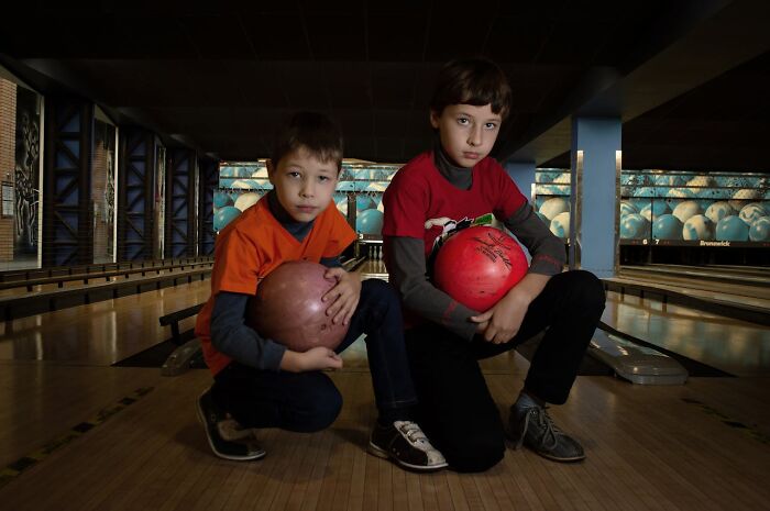 Two boys holding bowling balls at a bowling alley, capturing funny and clever moments in the heat of the moment.