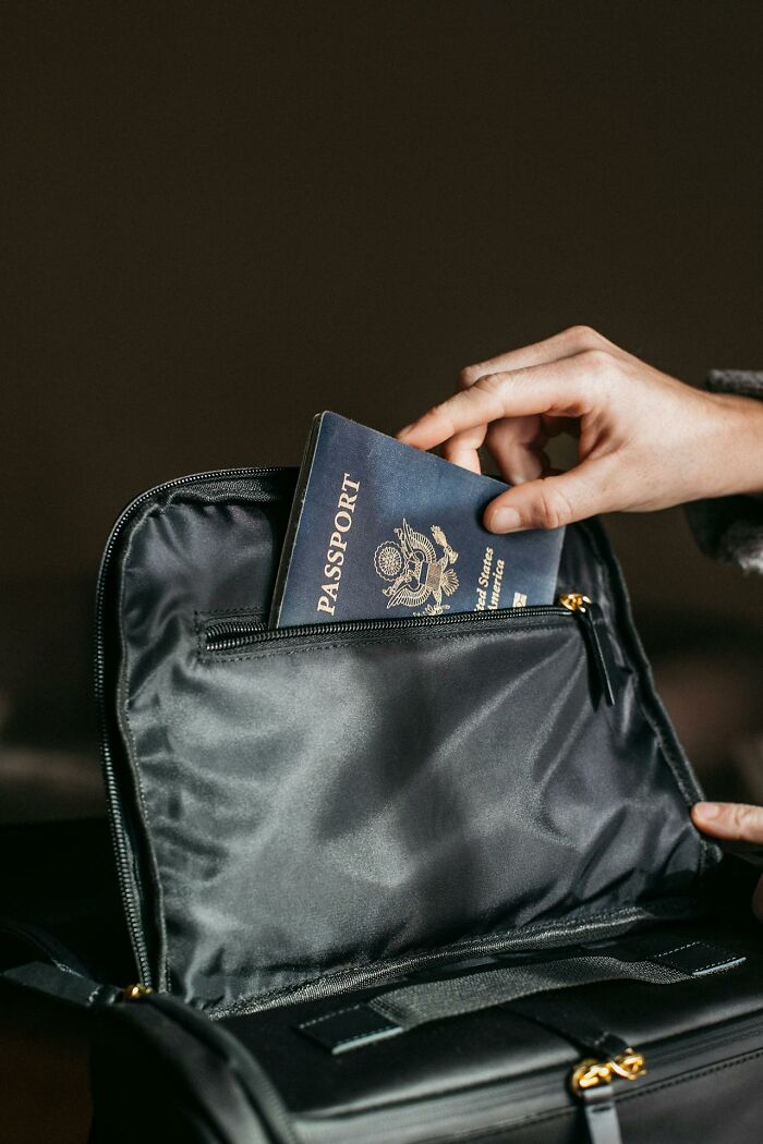 Hand placing a passport into a black bag pocket, illustrating unusual personal belongings left at lost and found.