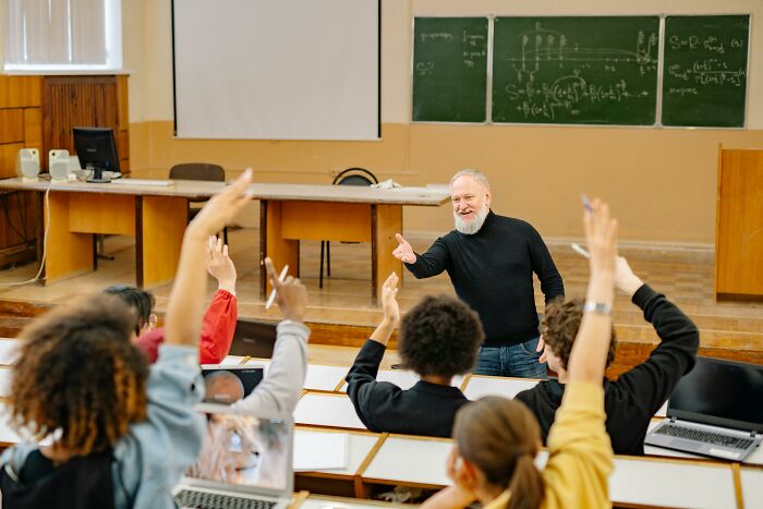 Teacher engaging with students raising hands in a classroom, illustrating employees revealing dark, dirty industry truths.