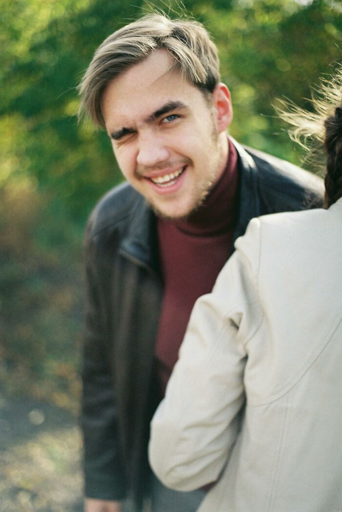 Young man winking and smiling outdoors, capturing a funny and clever moment in a casual setting.