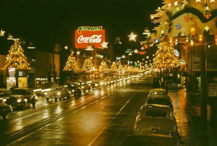 Historic nighttime street scene with classic cars and festive holiday lights, showcasing iconic historical pictures.