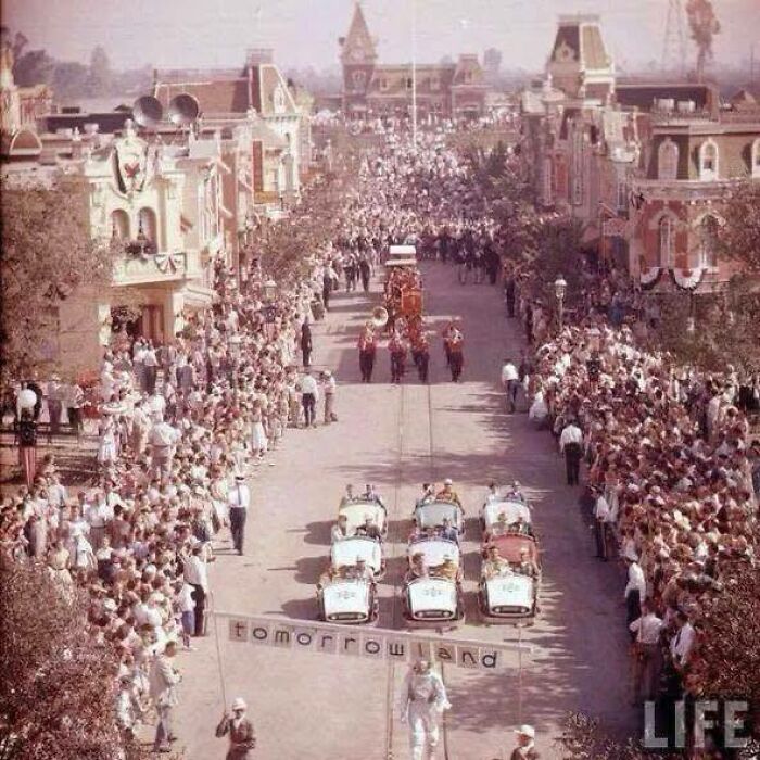 Classic and iconic historical photo of a crowded parade on Main Street USA with vintage cars and a marching band.