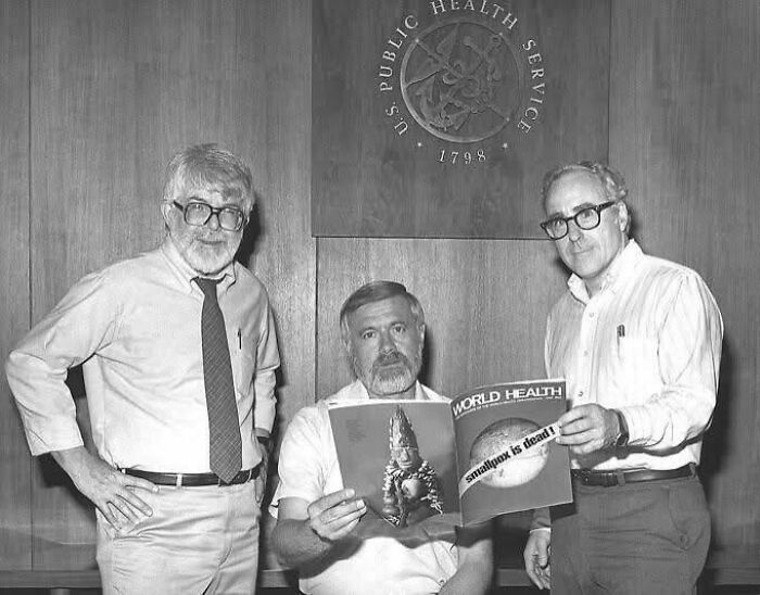 Three men in a health service office holding a World Health magazine announcing smallpox eradication, iconic historical picture.