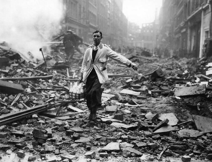 Man carrying milk bottles walking through rubble in a classic historical picture from one of the most iconic scenes ever taken.