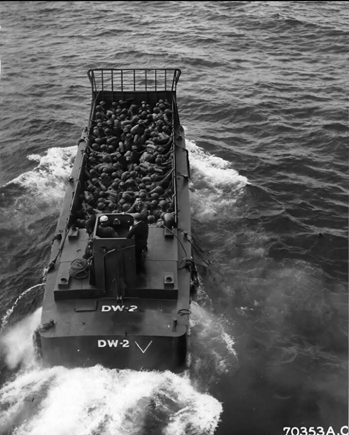 Black and white historical picture of a boat filled with soldiers navigating the ocean, classic iconic historical photo.