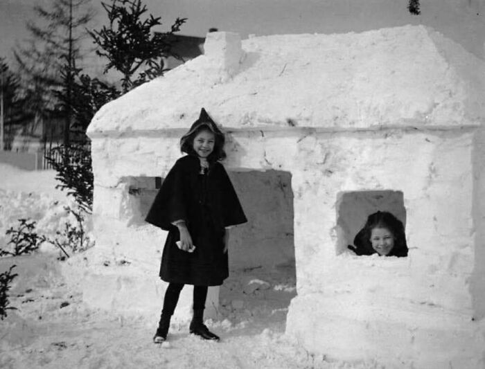 Two girls smiling by a snow house in a classic black and white historical picture from the most beautiful collection.
