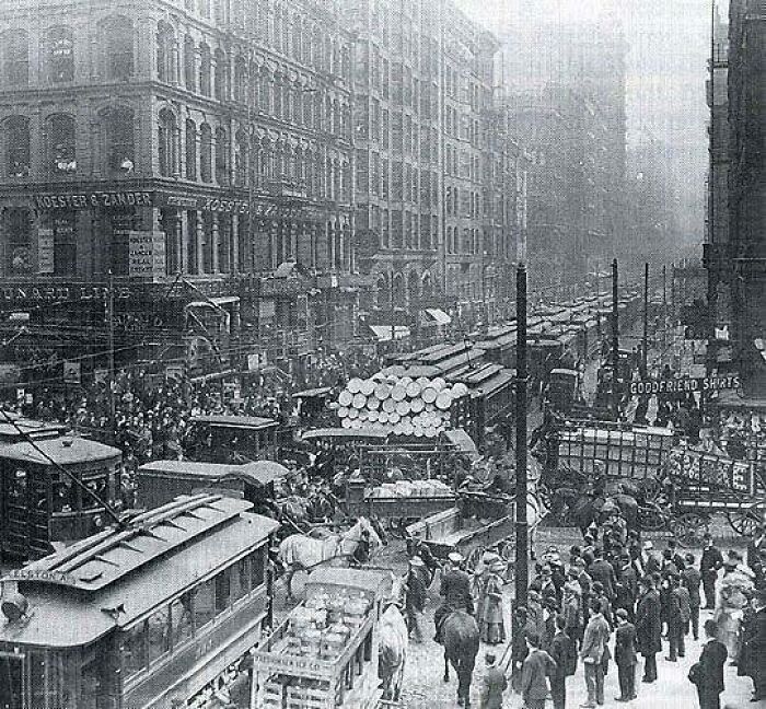 Historic bustling city street scene with horse-drawn carts and early trams in a classic historical picture.