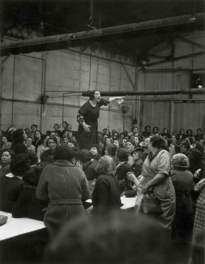Historic black and white photo of a woman speaking passionately to a large crowd, a classic and iconic moment captured.