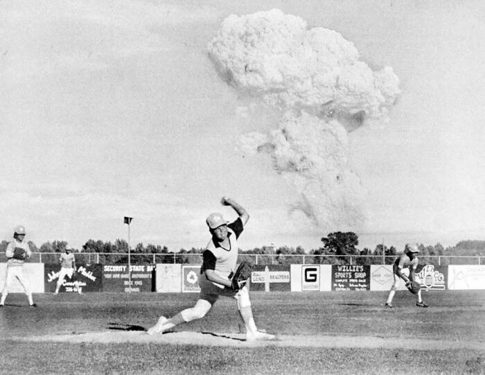 Baseball pitcher throwing ball on field with large explosion cloud in background, historical picture iconic moment