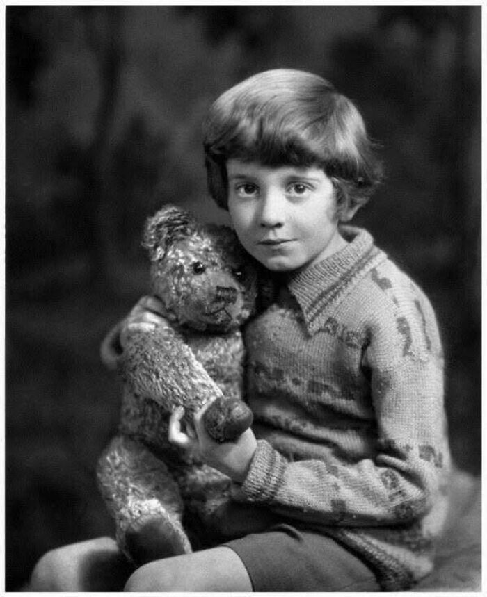 Black and white historical picture of a young child in vintage clothing holding a teddy bear, a classic iconic photo.