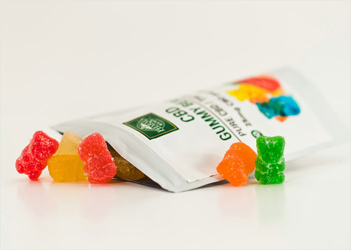 Colorful CBD gummy bears spilling out of a white pouch, relating to mom calls 911 after kids eat her gummies story.