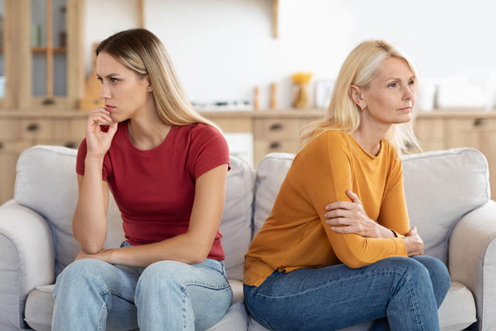 Two women sitting on a couch looking upset and distant, highlighting trauma from parents favoring polyamorous partners. Two women sitting on a couch looking upset and distant, highlighting trauma from parents favoring polyamorous partners.