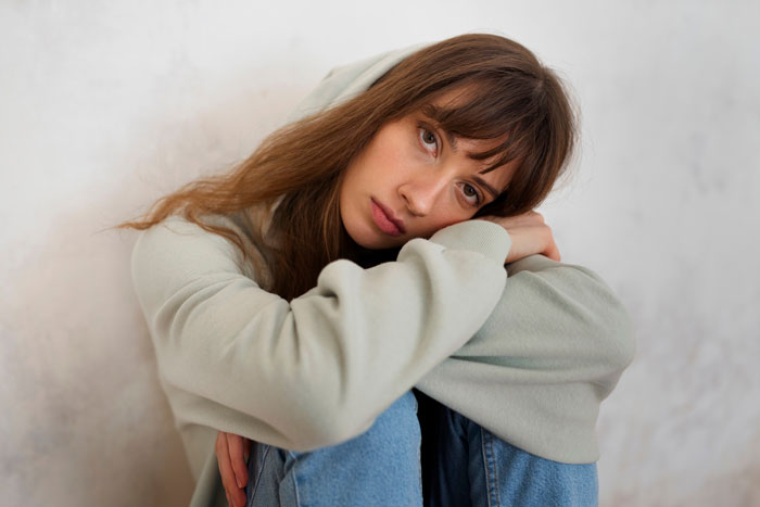 Sad young woman sitting alone hugging knees, reflecting trauma from parents favoring their polyamorous partners over their kid. Sad young woman sitting alone hugging knees, reflecting trauma from parents favoring their polyamorous partners over their kid.