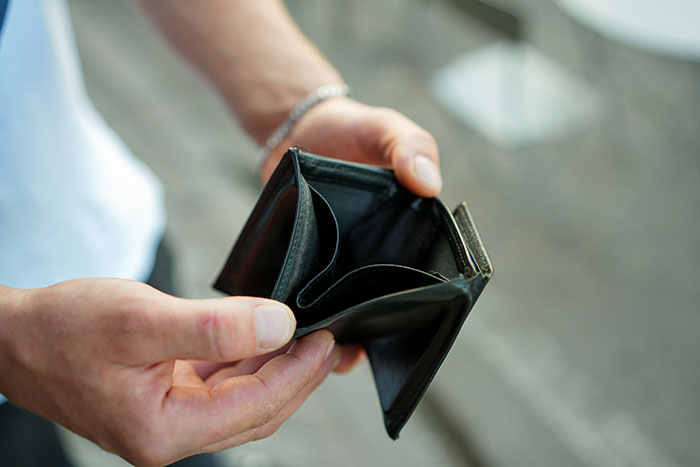 Person holding an empty black wallet showing poor person hacks to easily save thousands and avoid overspending habits.