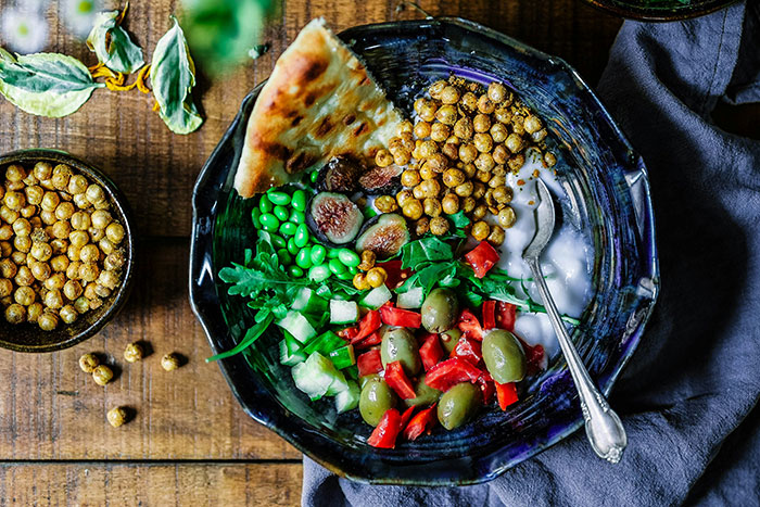 Bowl of healthy budget-friendly ingredients including chickpeas, greens, olives, and flatbread representing poor person hacks to save money.