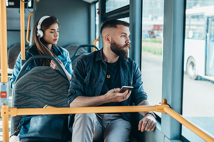 Young man and woman sitting separately on a city bus, illustrating poor person hacks to easily save thousands.