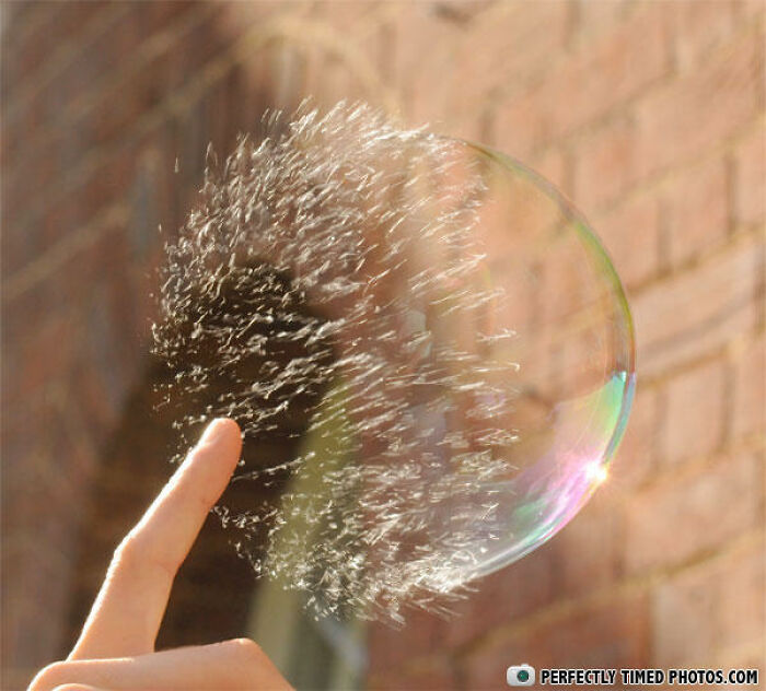 Finger popping a soap bubble captured in a perfectly timed photo showing the bubble bursting mid-air.