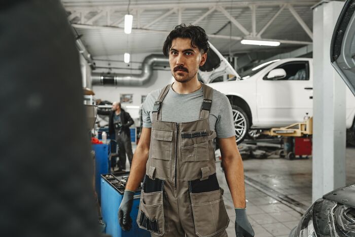 Man in mechanic overalls working in a busy auto repair shop showcasing incredible minds proving genius without a degree.