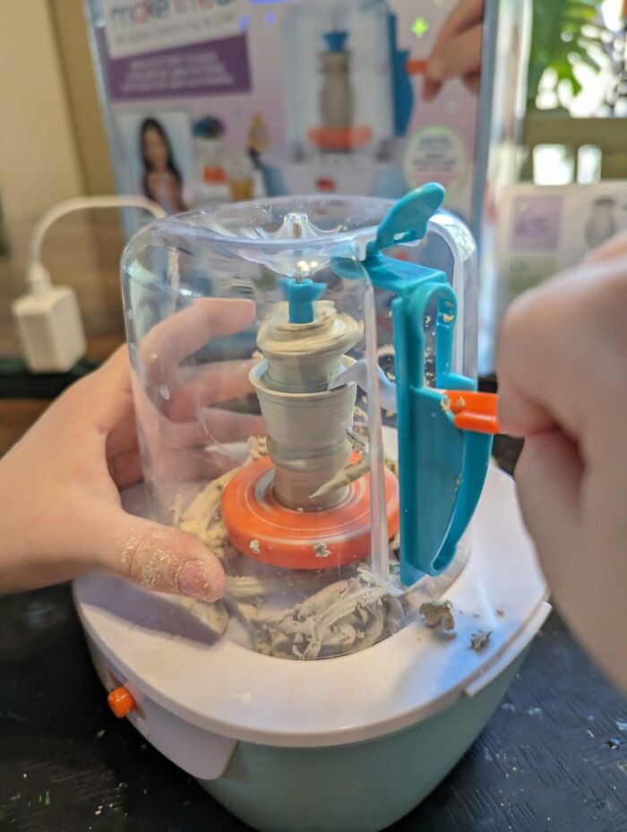 Child using a pottery wheel kit, shaping clay inside a clear plastic guard, a unique gift idea for creative projects at home.