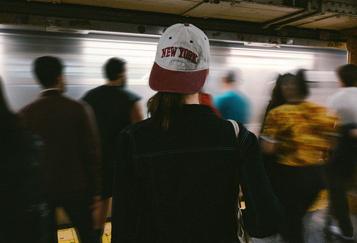 Woman wearing New York cap standing in a subway station among a crowd, symbolizing microfeminism clapping back at toxic masculinity.