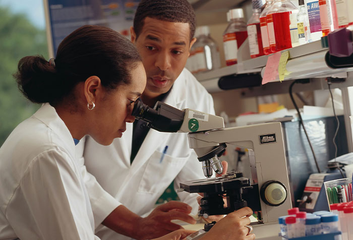 Two women scientists working with a microscope in a lab representing microfeminism challenging toxic masculinity.