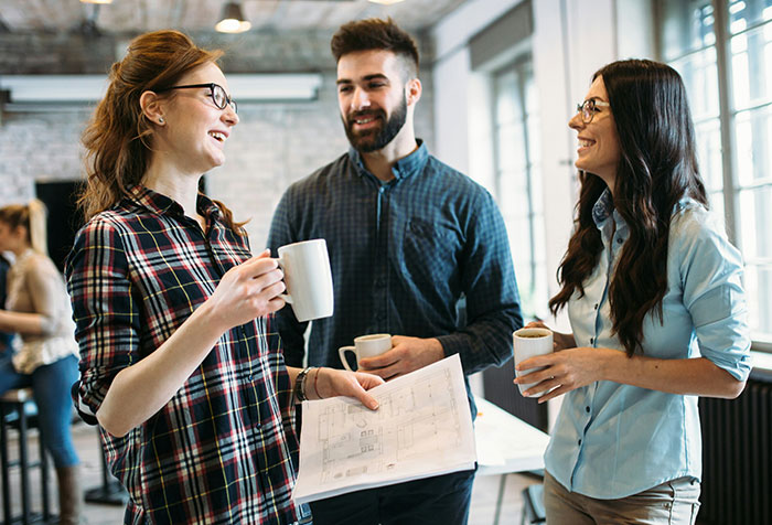 Three young professionals having a casual conversation holding coffee cups, illustrating women clapping back at toxic masculinity.