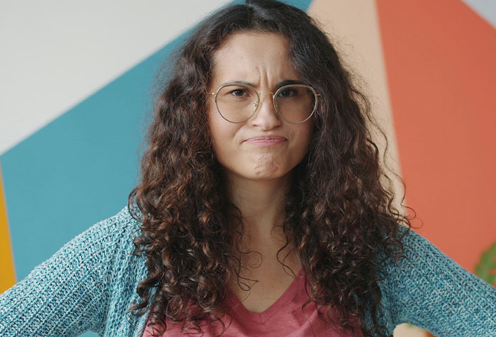 Young woman with curly hair and glasses looking defiant, expressing strength against toxic masculinity and microfeminism themes.