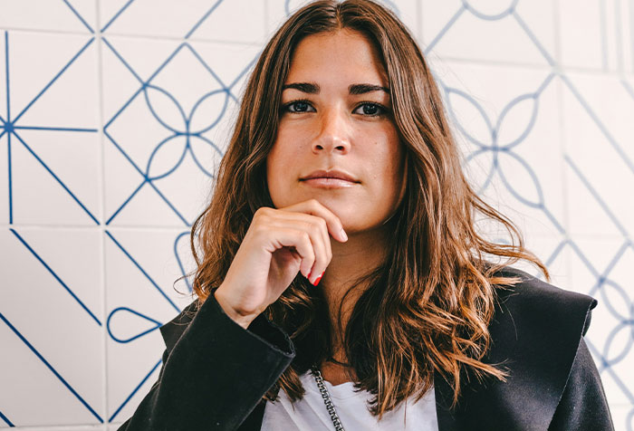 Confident woman with long hair posing thoughtfully against a patterned wall, representing acts of microfeminism.