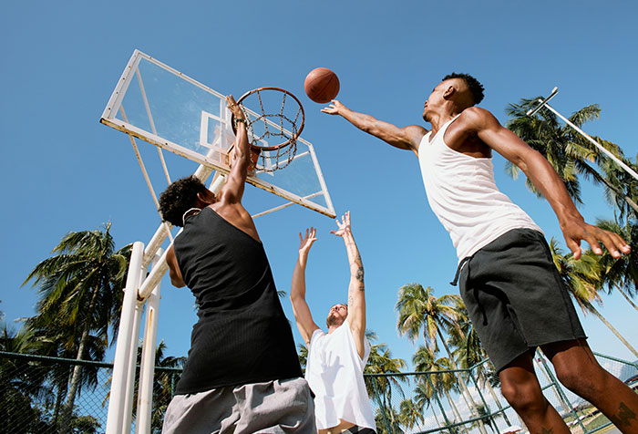 Young men playing basketball outdoors on a sunny day, illustrating themes of toxic masculinity and microfeminism debate.