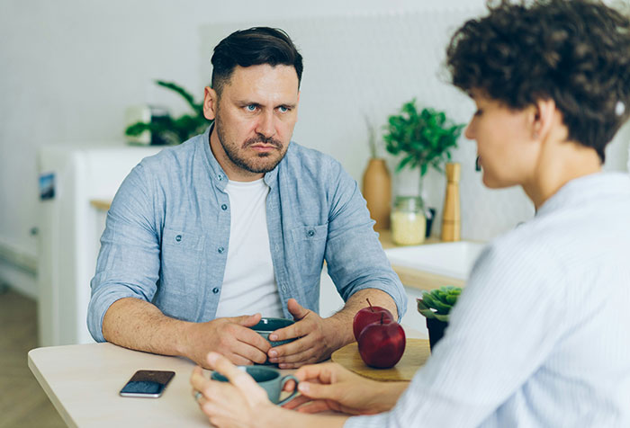 Two people having a serious conversation at a table, illustrating themes of toxic masculinity and microfeminism discussion.