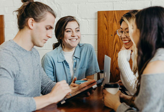 Four young women engaging in conversation and using digital devices while sharing acts of microfeminism together.