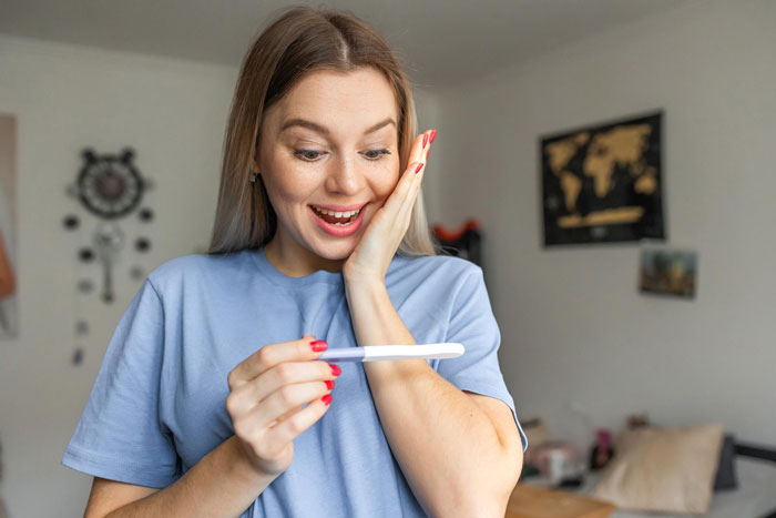Woman in blue shirt excitedly looking at positive pregnancy test showing desire for baby before turning 30. Woman in blue shirt excitedly looking at positive pregnancy test showing desire for baby before turning 30.