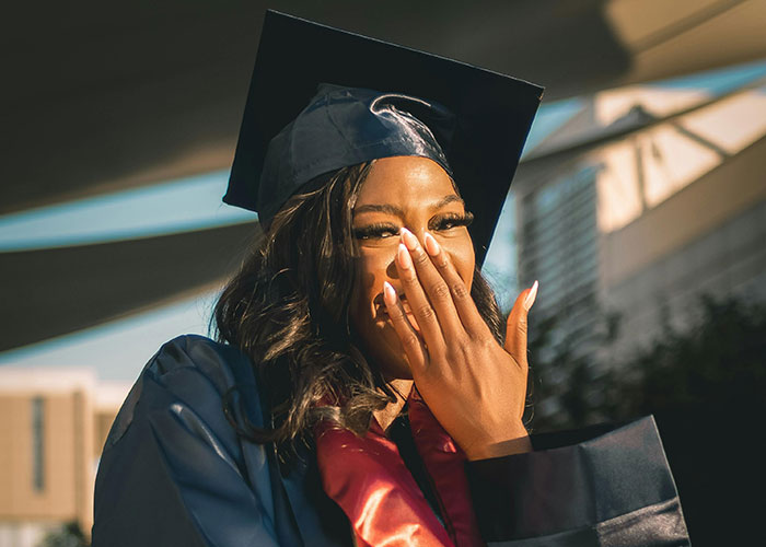 Young woman in graduation gown and cap smiling and covering her mouth, symbolizing surprising facts about prison life.
