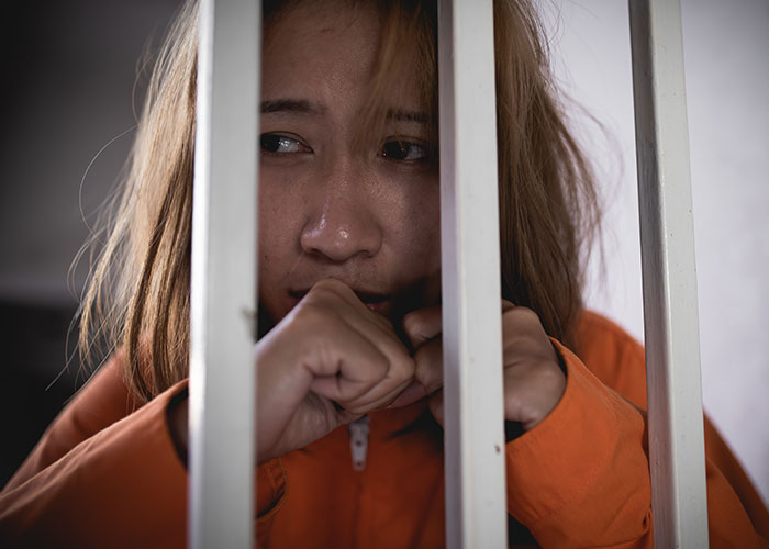 Young inmate in orange prison uniform looking anxious behind bars, illustrating surprising facts and misconceptions about prison life.