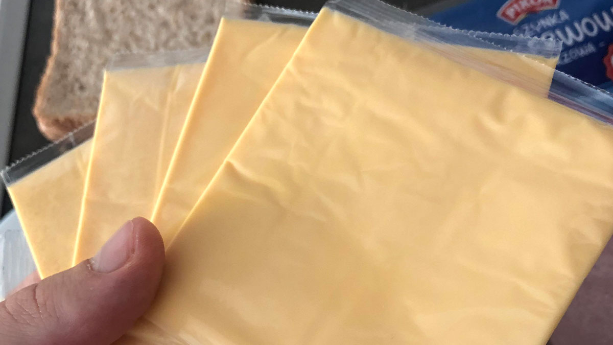Close-up of a hand holding multiple individually wrapped American cheese slices at a kitchen counter.