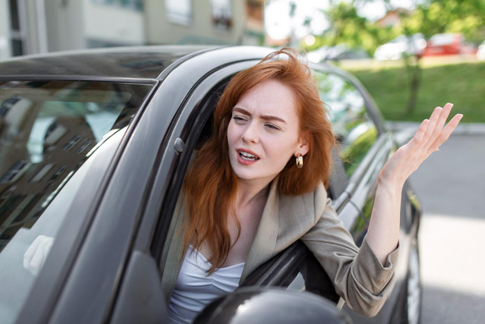 Frustrated woman leaning out of car window, upset about entitled neighbor driving over yard without care.