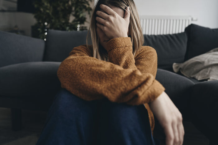 Woman sitting on the floor covering her face, depicting stress and common habits wrecking your health long-term.