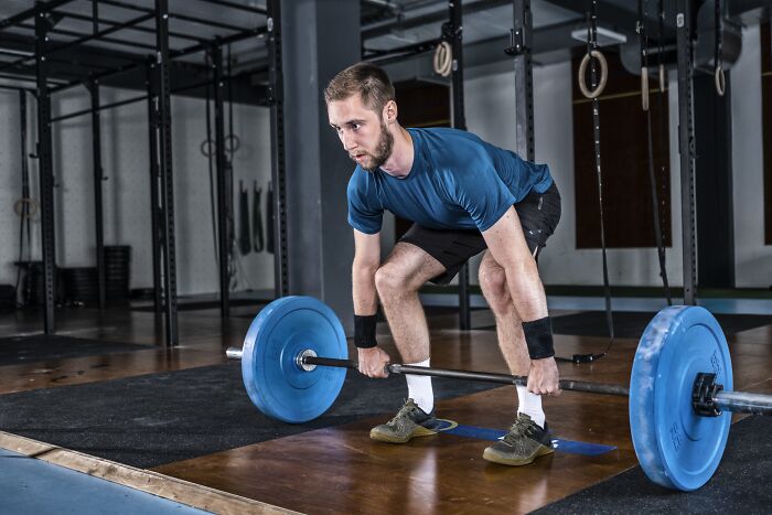 Man lifting a barbell in a gym, demonstrating common habits that might be wrecking your health long-term.