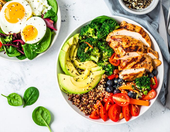 Healthy grilled chicken bowl with avocado, broccoli, quinoa, tomatoes, and berries emphasizing long-term health habits.