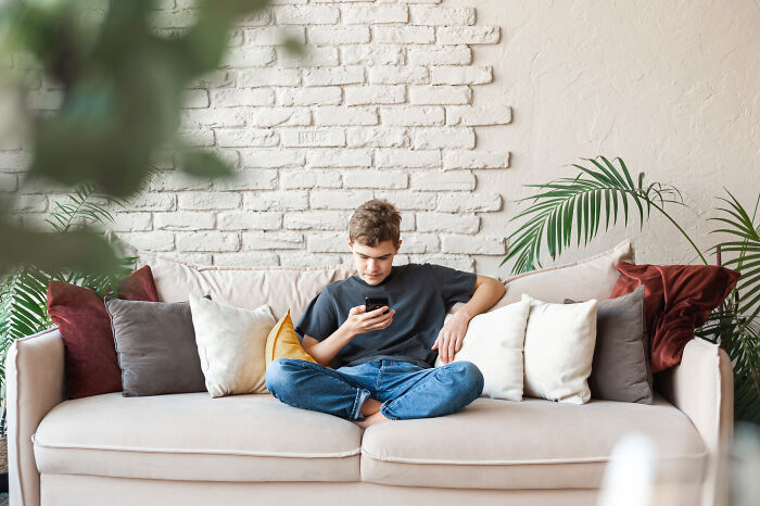 Teenage boy sitting on a couch looking at phone, illustrating common habits that might be wrecking your health long-term.