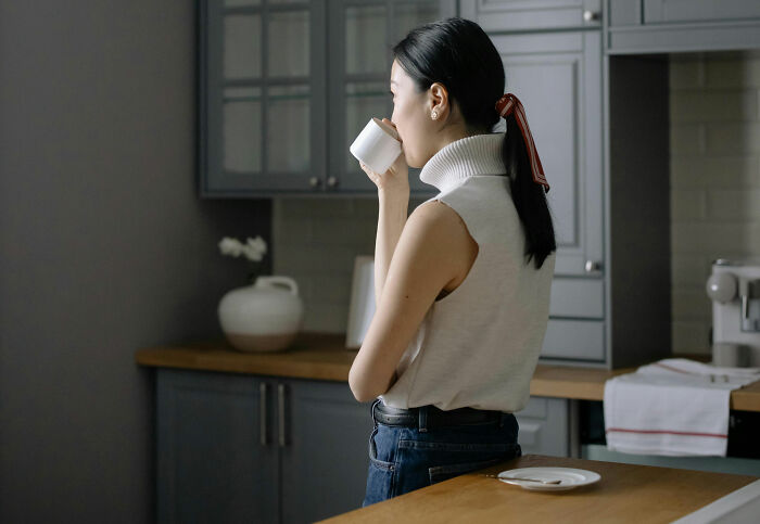 Woman in a modern kitchen sipping from a cup, reflecting on common habits that might be wrecking long-term health.
