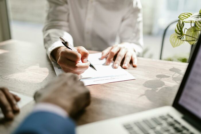 Person signing a resignation letter at a desk with laptop and plant, illustrating quitting jobs in record time.
